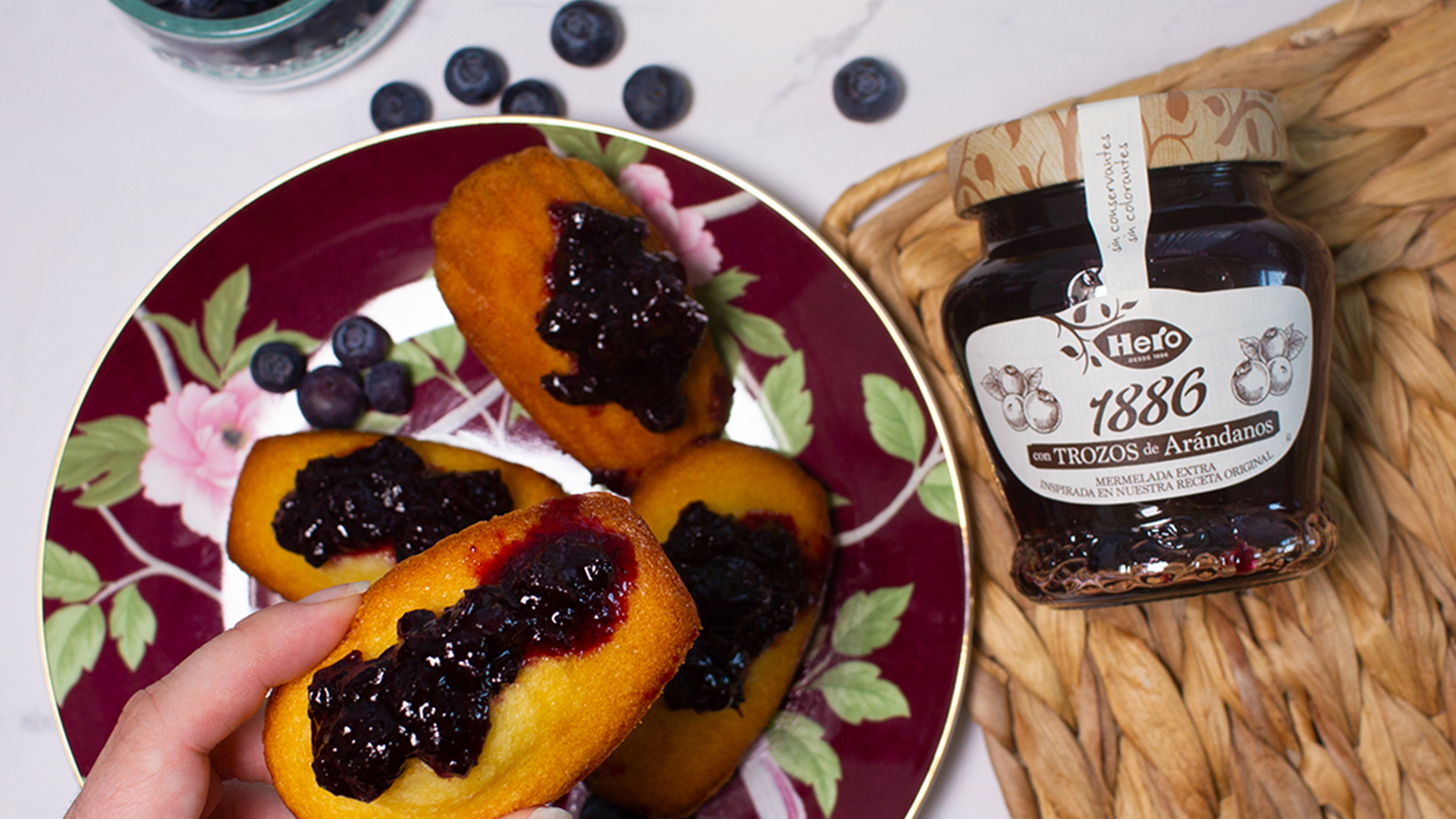 a hand picking up a cake with jam from a plate